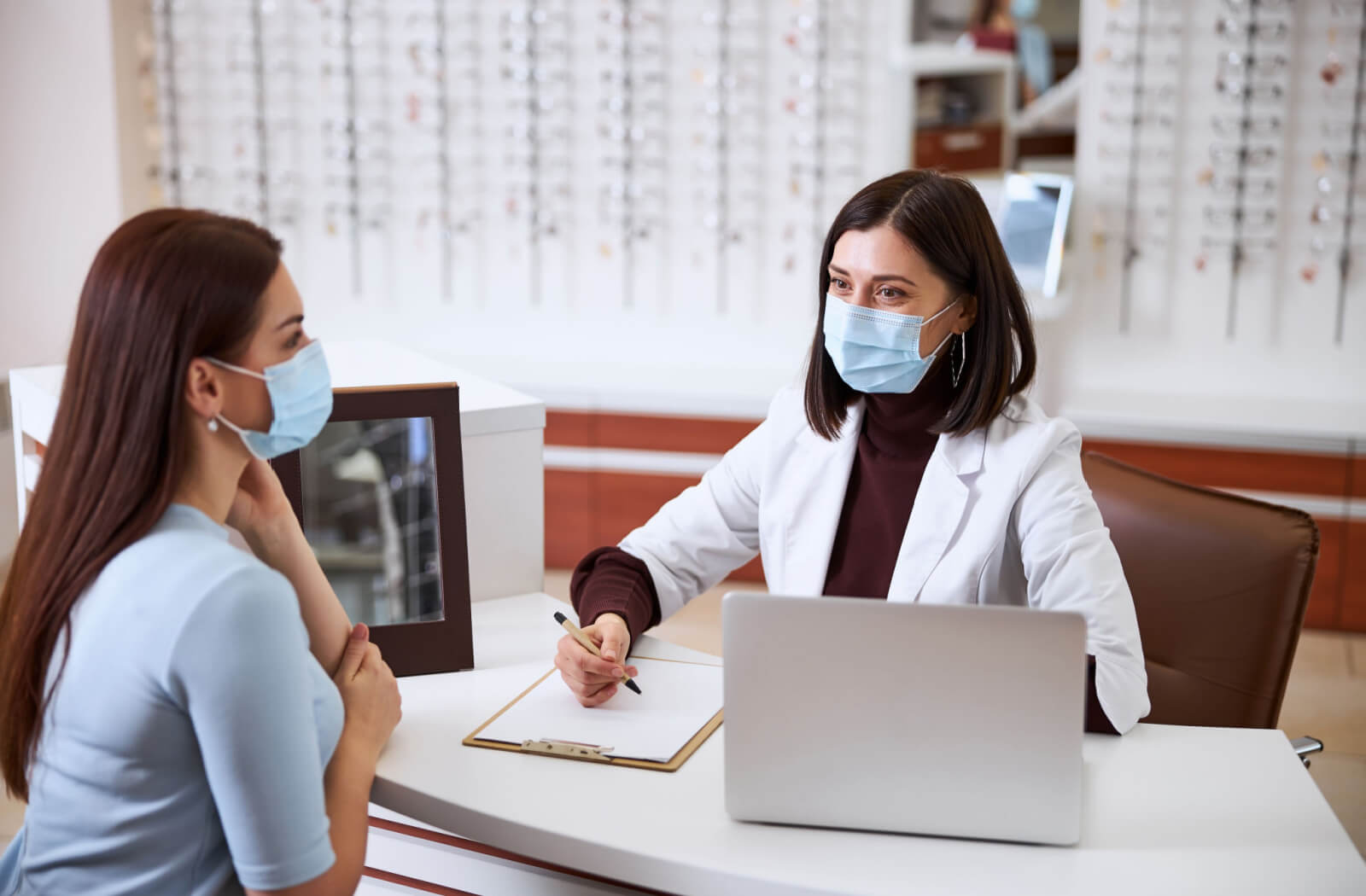 A female optician is interviewing a female patient in her clinic with various questions about their general health, medical history, and family medical history.