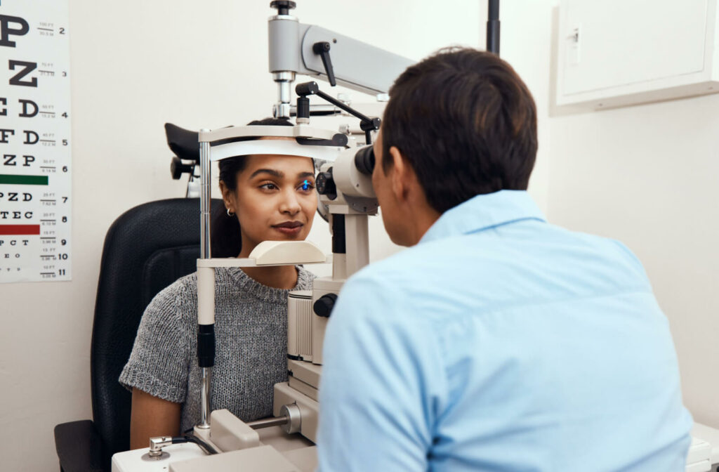A young woman getting her eyes examined with a slit lamp by an optometrist.