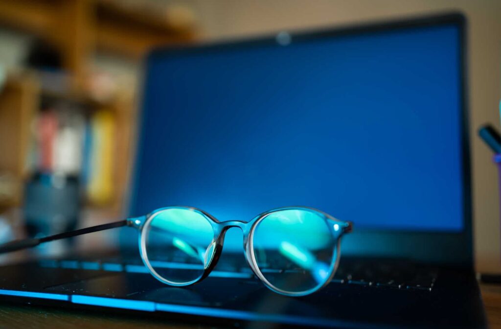 A pair of blue light glasses sitting on the keyboard of a laptop