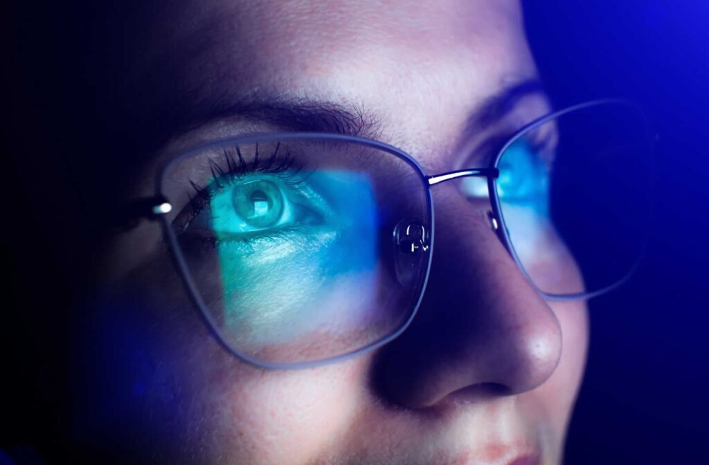 A close up of a woman wearing blue light glasses with a reflection of a screen in the lenses
