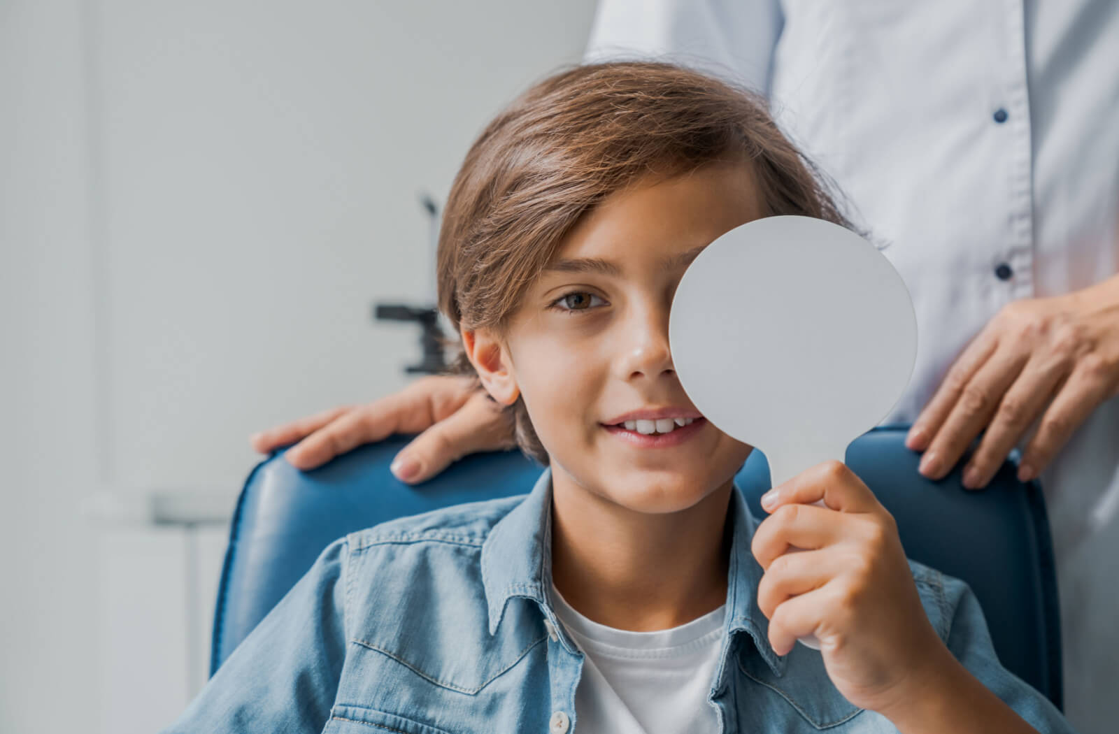 A boy is covering his eye with a medical tool for checking visual acuity in an optical clinic.