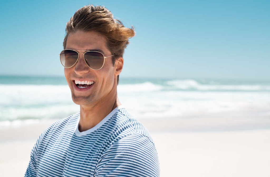 A happy young man wearing a pair of polarized sunglasses at the beach to protect his eyes from the sun.