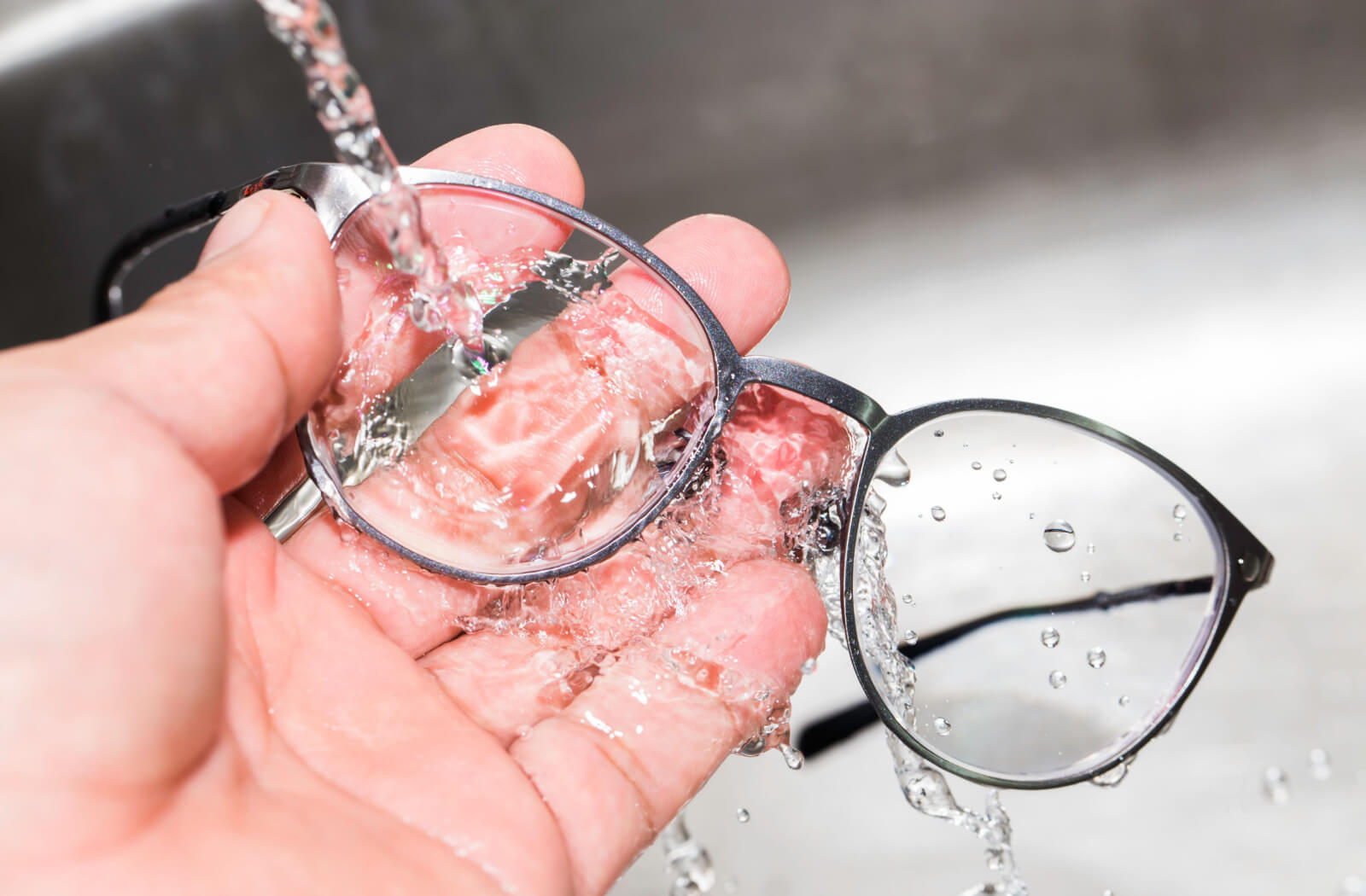 A person rinsing their glasses with water in their sink.
