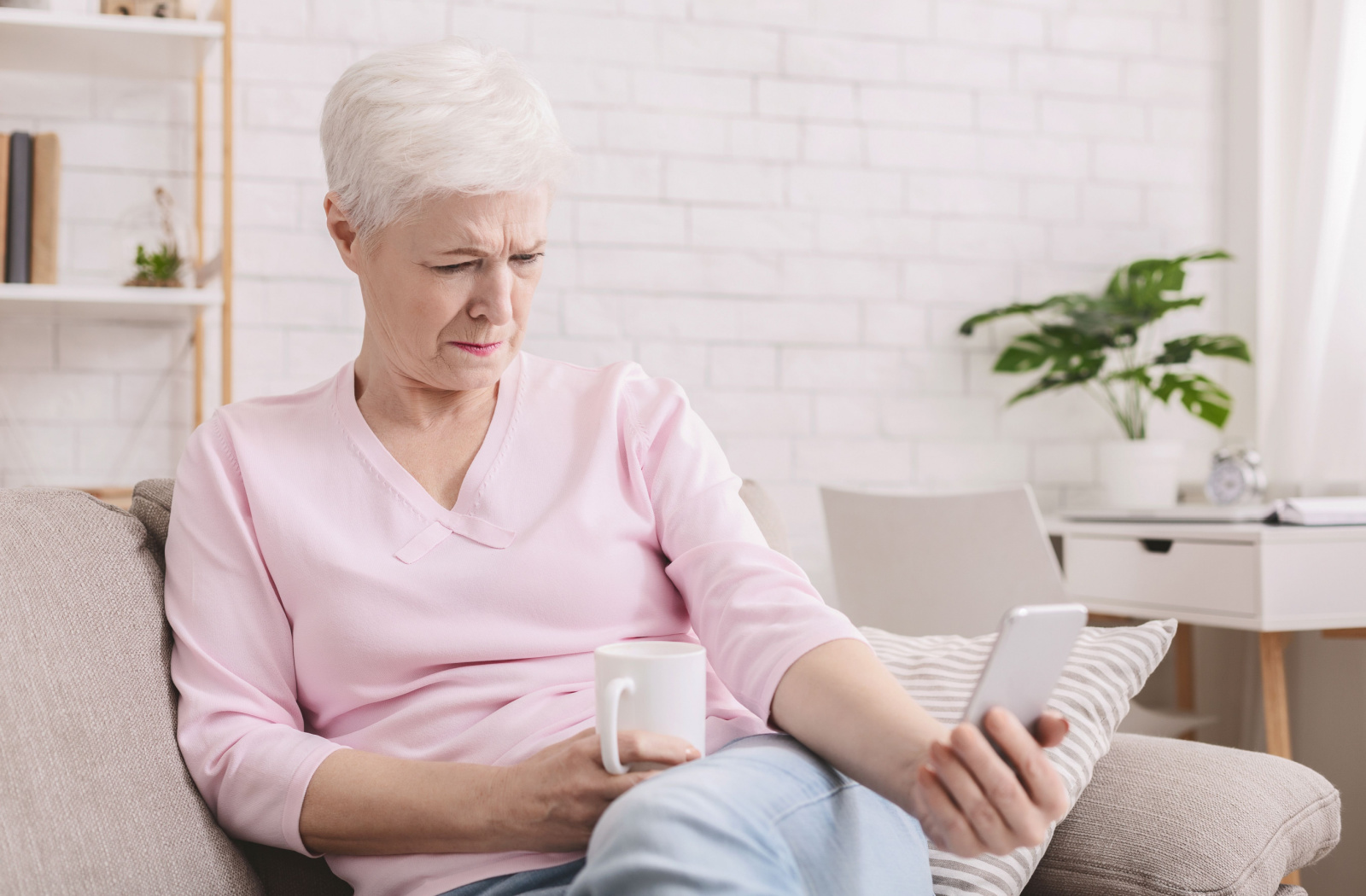 A senior woman in a pink top holding her phone further away from her to see its content better.