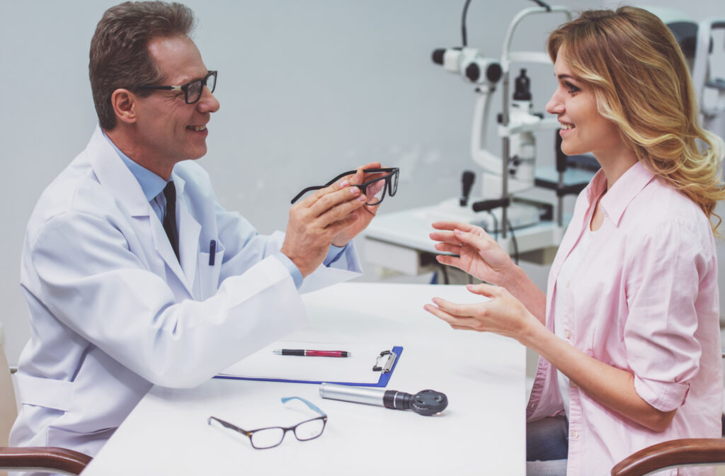 An optometrist presenting a pair of eyeglasses to his patient for her to try on.