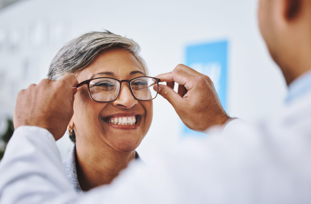 A woman smiling while at an eye exam getting glasses fitted.