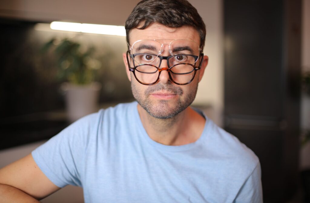 A person wearing 3 pairs of different glasses on their face stares into the camera.