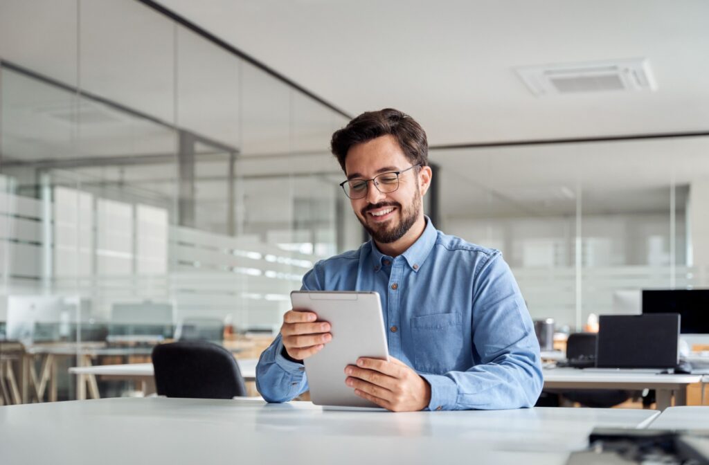 A person sitting at work reads from their tablet thanks to their accurate prescription glasses.