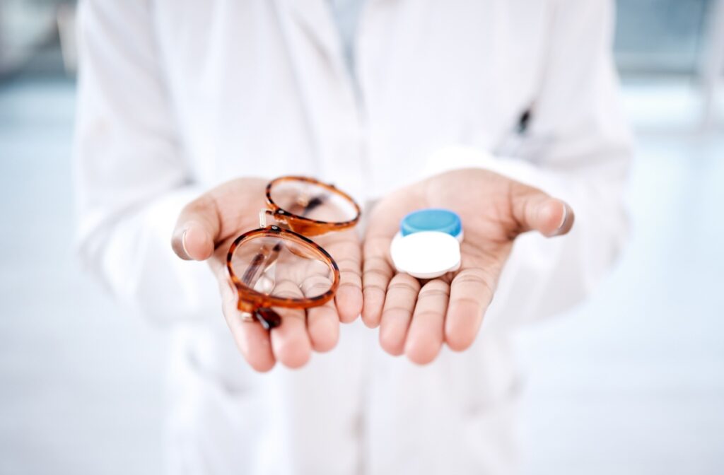 Someone holds a pair of glasses and a contact lens case on each hand