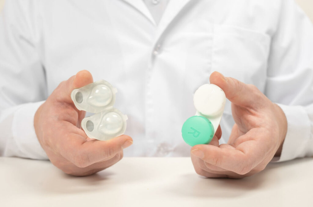 An optometrist holds two contact lenses cases, one containing disposable lens, the other containing reusable lenses.