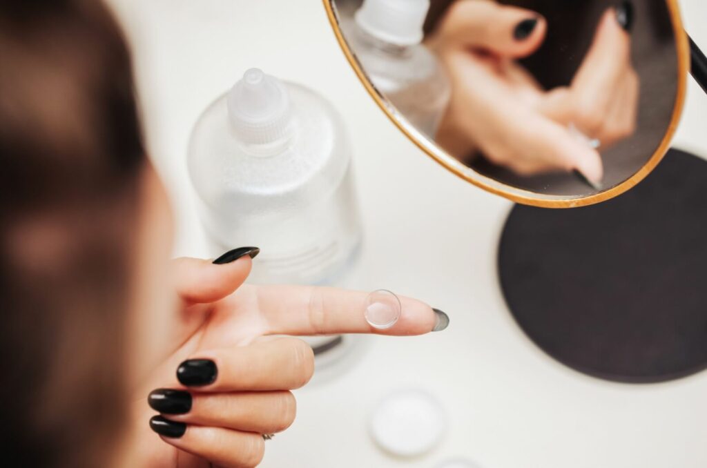 A person holds a single contact lens on their index finger as they prepare to clean it with proper contact solution.