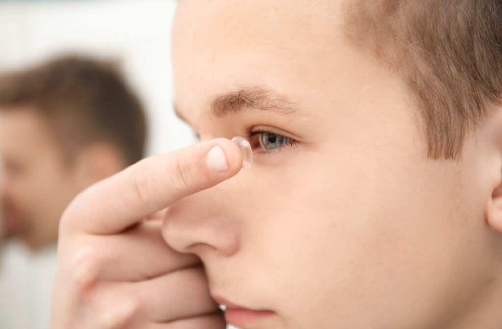 A close-up side profile of a teenage boy carefully placing a clear MiSight contact lens onto his eye, demonstrating a simple daily routine for pediatric myopia management.