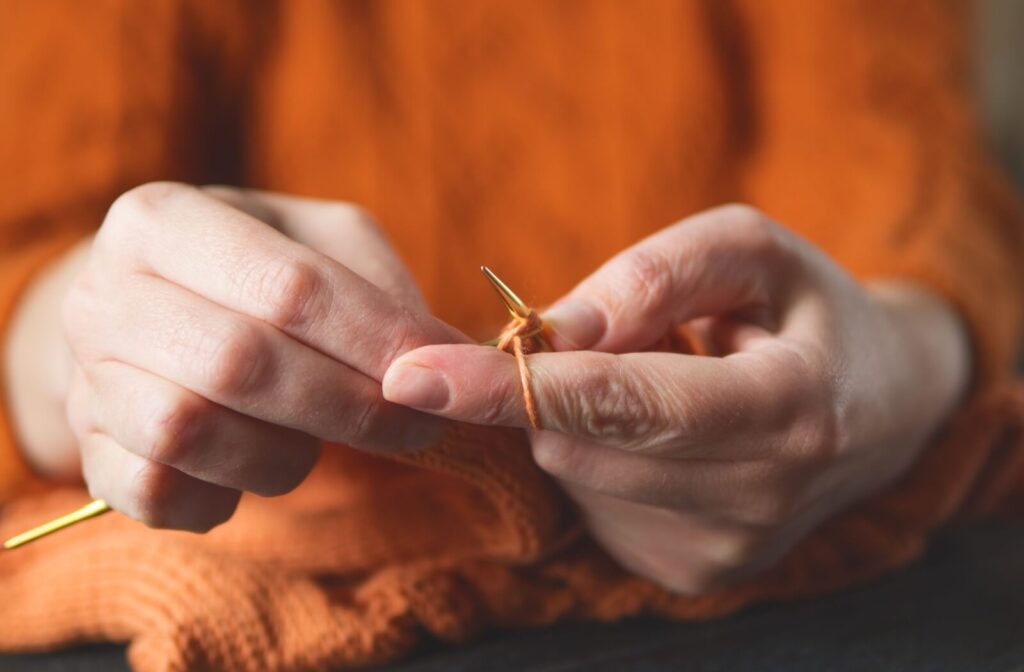 Close-up of hands knitting with orange yarn to practice fine motor skills.